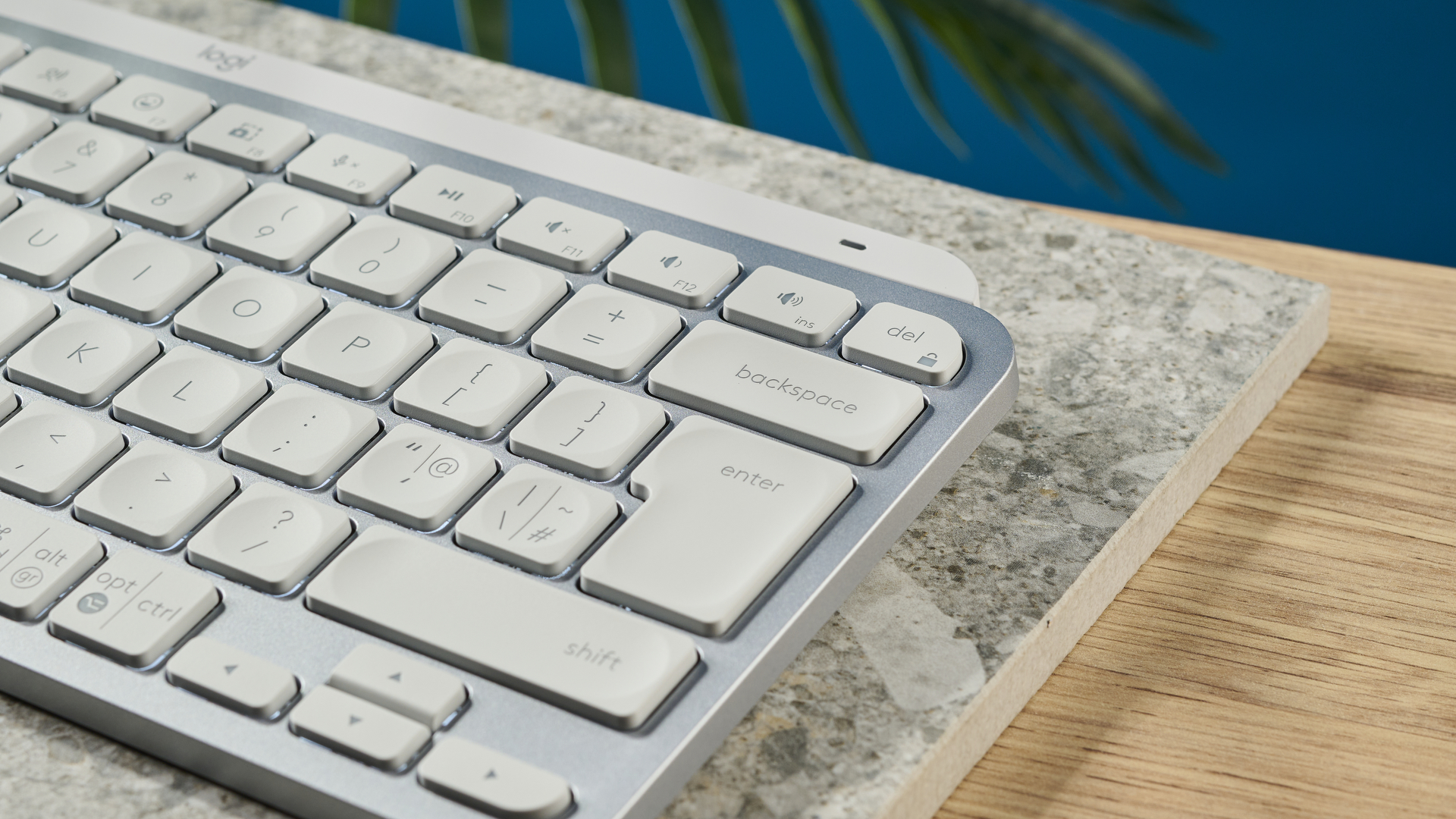 Una fotografia della Logitech MX Keys Mini in grigio chiaro, posizionata su una lastra di pietra con una parete blu sullo sfondo.